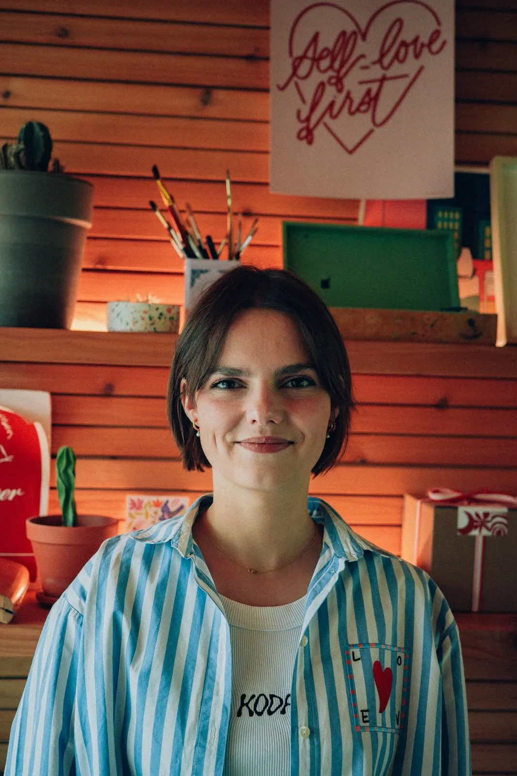 Nora Wansart dans son atelier, devant des étagères de pinceaux, de cactus et de posters calligraphiés